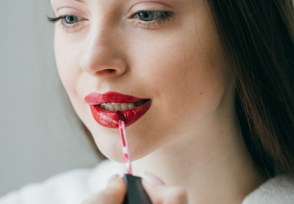 Closeup shot of woman paint her lips by cosmetic brush lipstick on lips. Studio shot. Lip gloss.