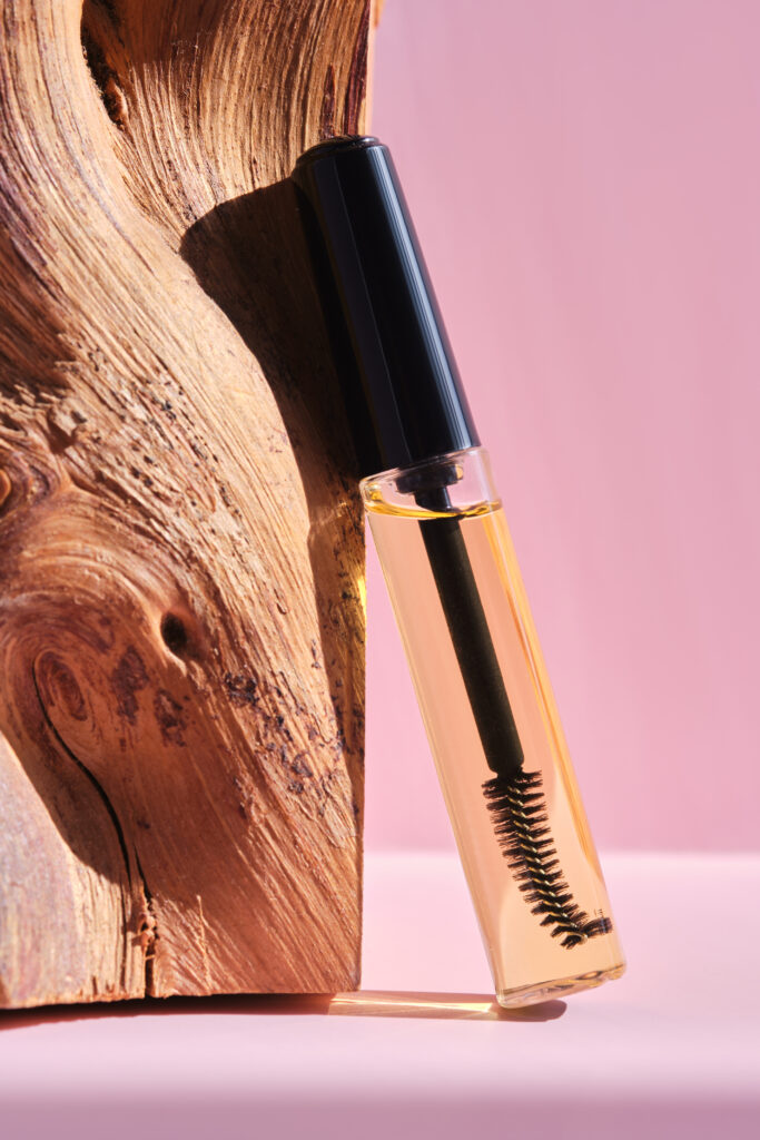 Cosmetic oil for the growth of eyebrows and eyelashes with a comfortable brush on a pink background.