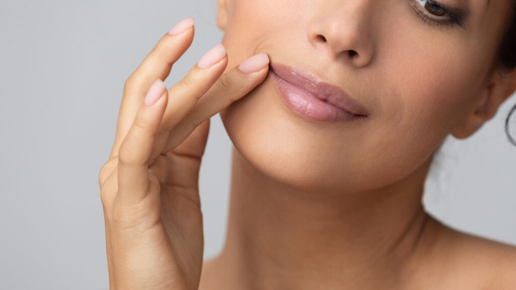 Cosmetology concept. Girl holding hand near lips, grey background.