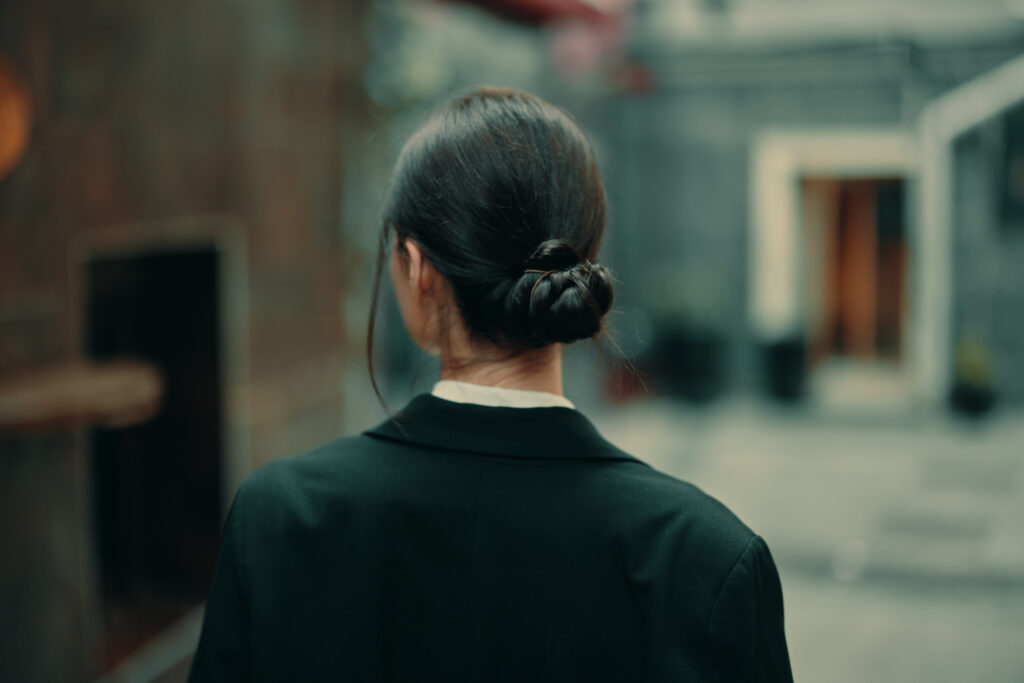 classic low bun hair. black bun hair. stylish woman in a black jacket walks along the city street with her back to the camera, follow me. High quality photo