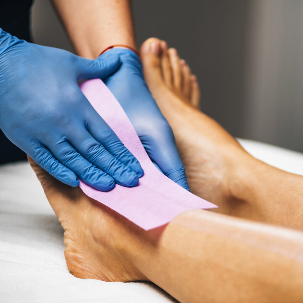 Waxing - Beautician Removing Unwanted Hair from Female Leg with Wax Strips.