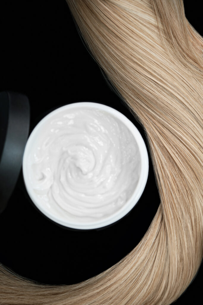 A strand of blond hair with hair balm on a black background. Close-up. hair mask