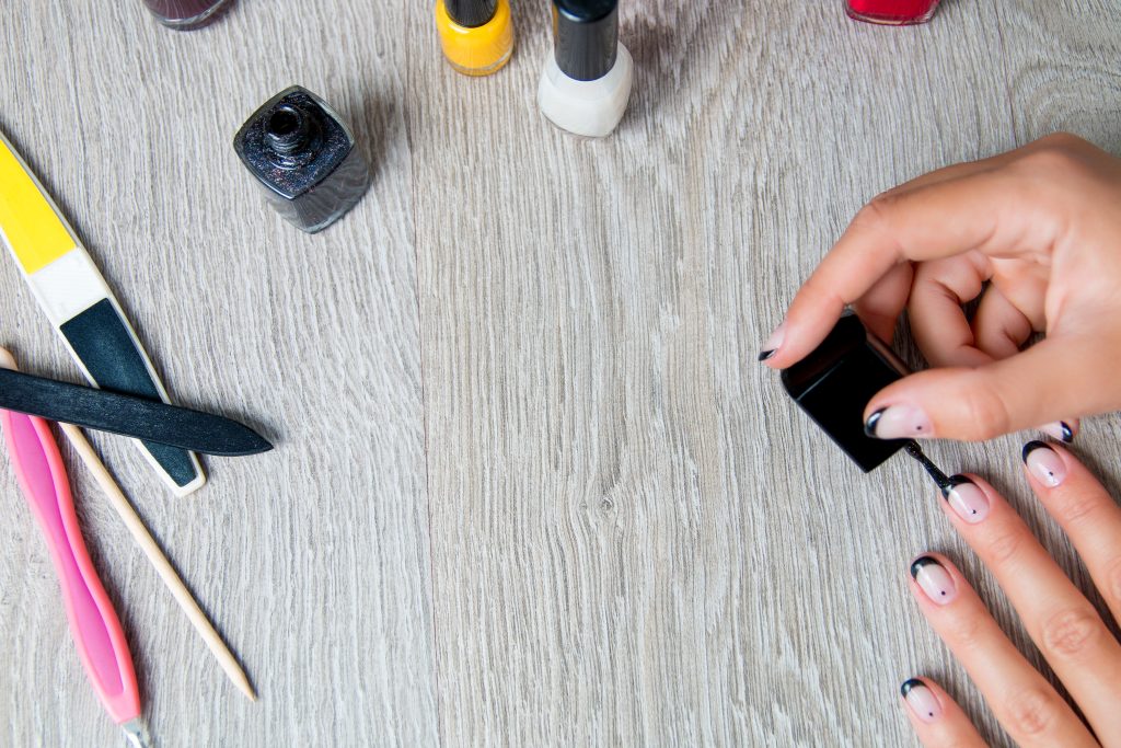 Black nail polish being applied to hand with tools for manicure on background. Beautiful manicure process.  Top view. Copy space. Frame. nail care. nail french tips