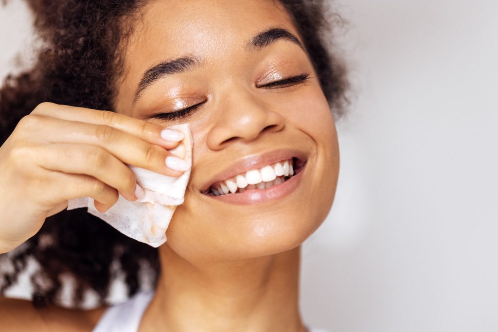 makeup removers. Close up of face of young happy attractive african washing off her makeup. Charming smiling mixed race girl wipes her face skin with napkin. Young beautiful woman closed her eyes. Skin care concept.