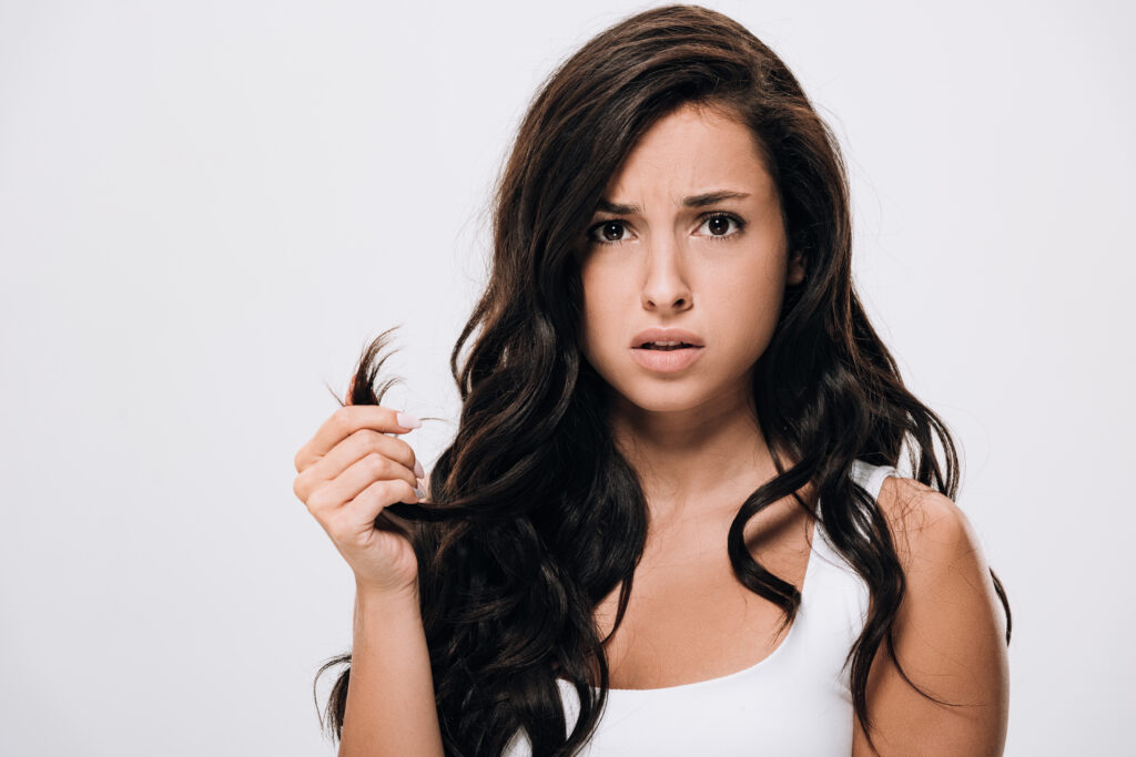 confused brunette beautiful woman showing damaged hair isolated on grey. Hair Split Ends Treatment