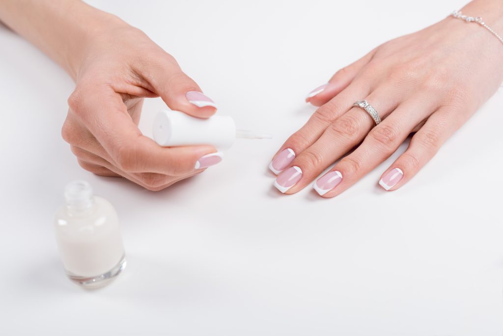 cropped shot of woman holding nail polish while doing manicure. home nail care. DIY nail care.