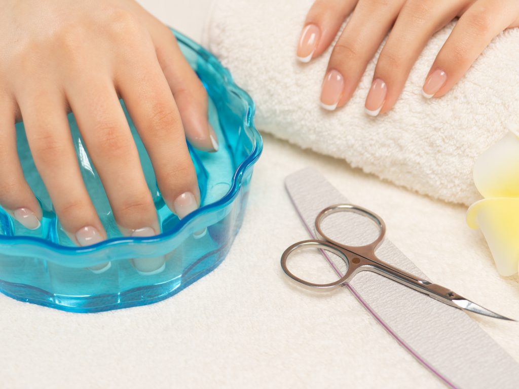 Soak in Warm Soapy Water. Woman gets manicure procedure. Beautiful female hands. Hand care. Woman cares for the nails on hands. Beauty treatment with skin of hand.   Woman's hands close-up view.