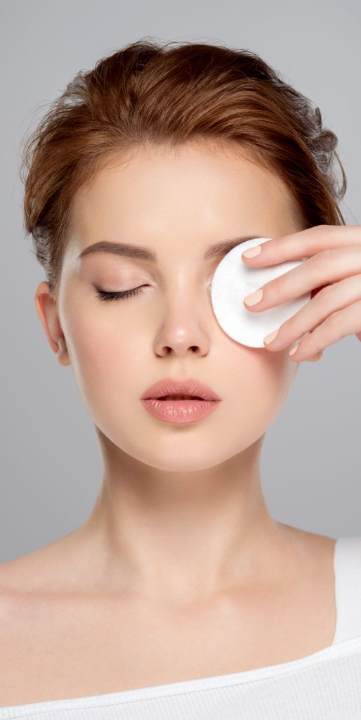 Beautiful face of a young Caucasian woman with a cotton pad in her hand, isolated.   Pretty white model takes care of her face. Removing makeup with a cotton swab