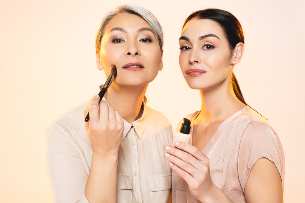 beautiful multicultural women holding cosmetic brush and makeup foundation isolated on beige. foundation secrets. applying foundation. makeup. face. foundation.
