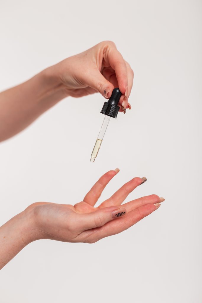 Cuticle Nail Treatment. Female hands holding drops of cosmetics oil with a pipette and doing hand skin care, close-up. Beauty and health, skin care.