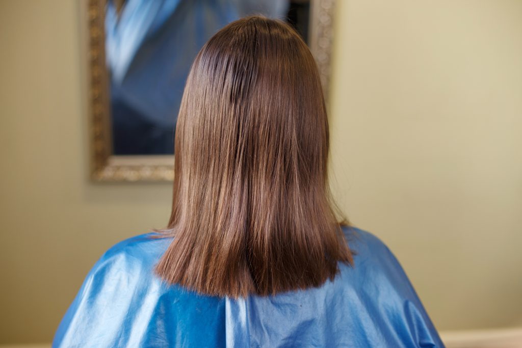 brunette woman with shiny brown straight hair back view in salon. Managing Growth Expectations. Easy Tips for Growing Out Short Hair at Home