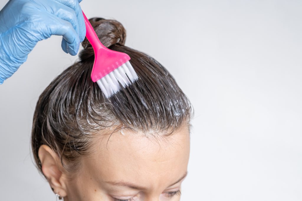 Close-up of a woman's heClose-up of a woman's head in the process of hair coloring on a white background. Closeup woman hands dyeing hair using a brush. Colouring of white hair at home. hair coloring. dye hair. home hair coloring.