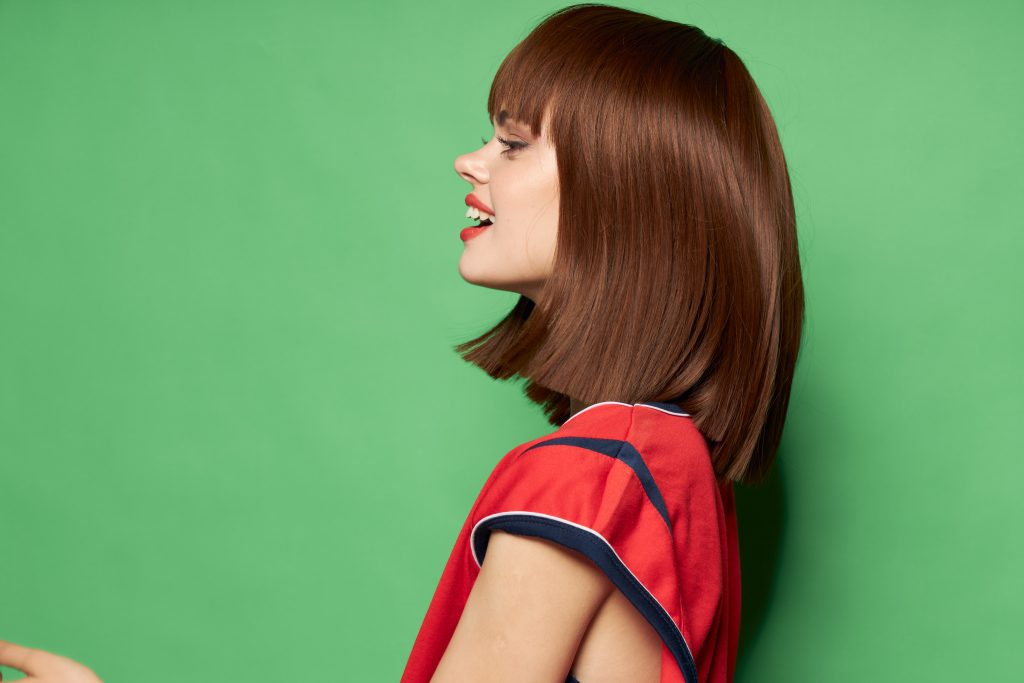 free place Green background beautiful woman in red t-shirt side view. Growing Out Short Hair