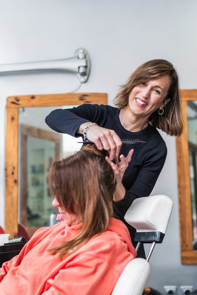 Trim Your Hair Regularly for Healthy Growth. A hairdresser smiles while styling a client's hair in a modern salon. The interaction is friendly and professional. Concept of cheerful salon service.