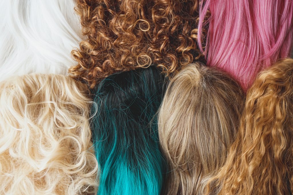 Image of assorted wigs of different styles and colors included dyed, curly and natural hair styles. different hair colors. different hair dies.