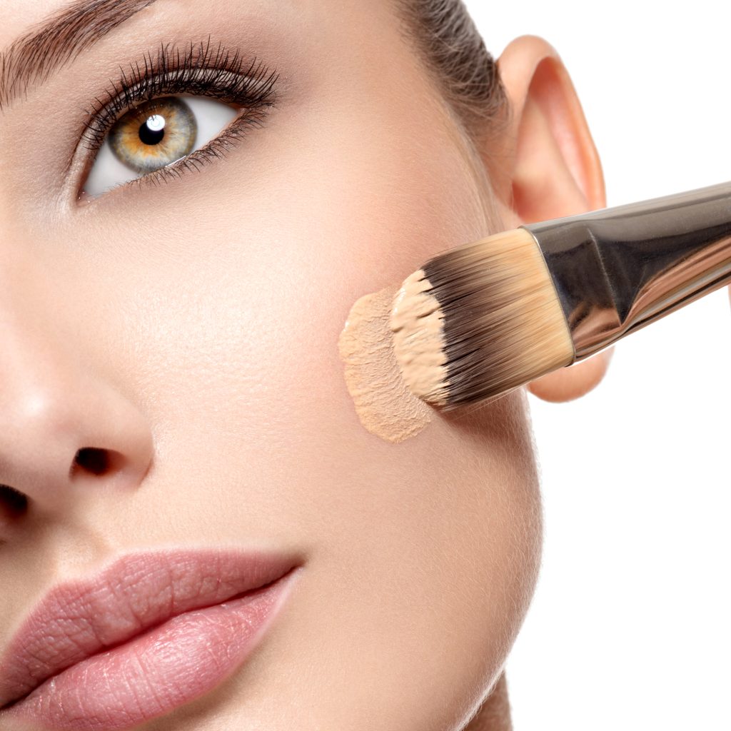 Makeup artist applying liquid tonal foundation  on the face of the woman. Closeup photo of cheek