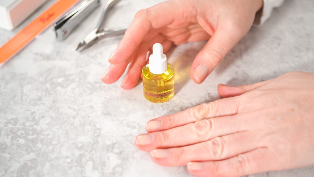 Woman finishing her manicure at home with simple manicure tools. Applying cuticle oil around nails.