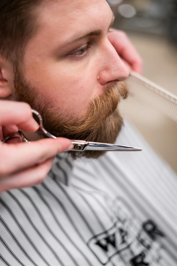 beard care. home beard care. A white blonde man with trimmed beard. a scissor and a comb next to his beard.