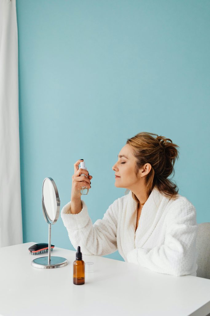 A beautiful woman is preparing to apply makeup, spraying her face before she starts. The wall behind her is blue. face care. face moisturizer.