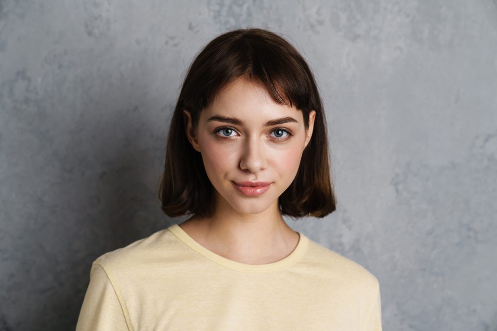 Trust the hair Growth Process. Growing Out Short Hair. Portrait of a beautiful smiling young girl in casual clothes standing isolated over gray background, close up