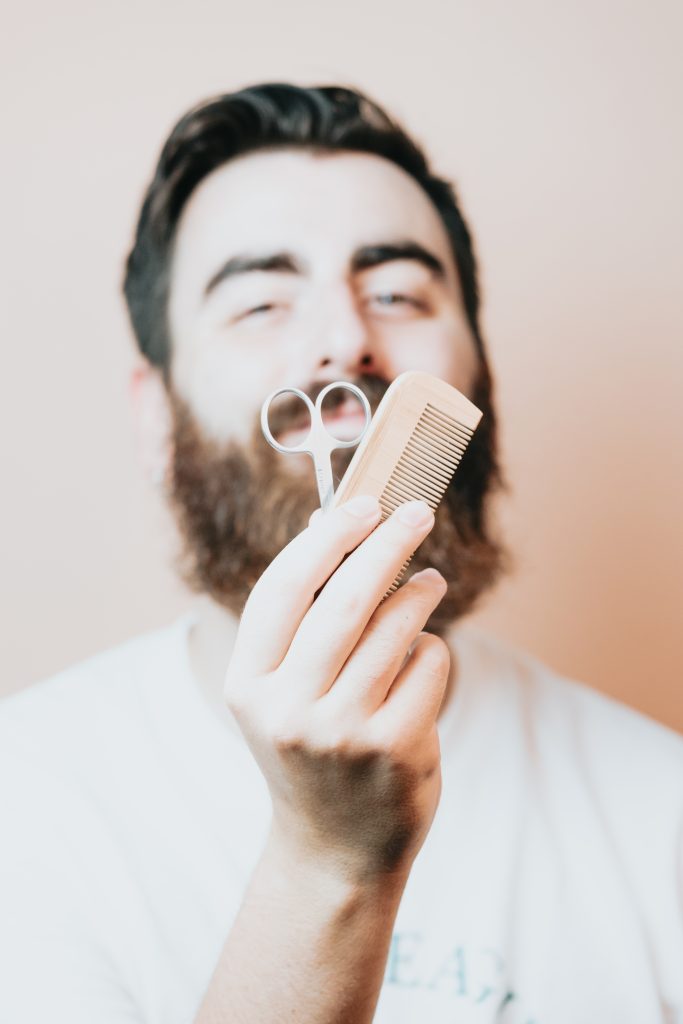 Portrait of bearded barber holding equipments in hand, looking at camera, isolated on pastel background. Step 5: Brushing and Combing.