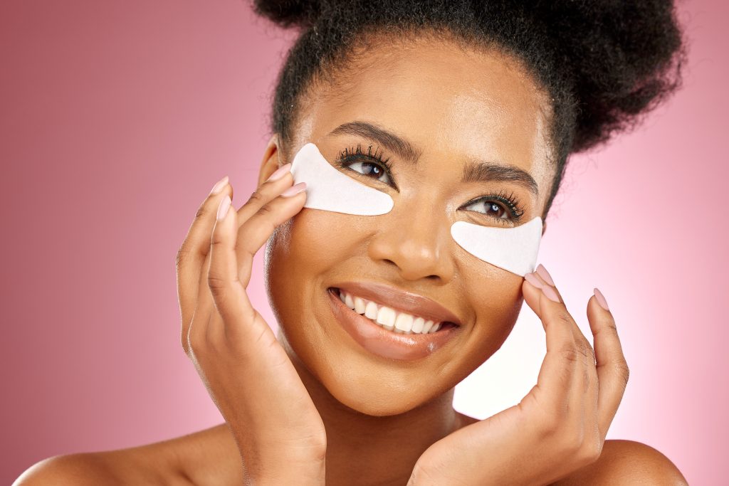 Skincare, face and black woman with mask on eyes, cosmetics and dermatology on pink background. Bea..