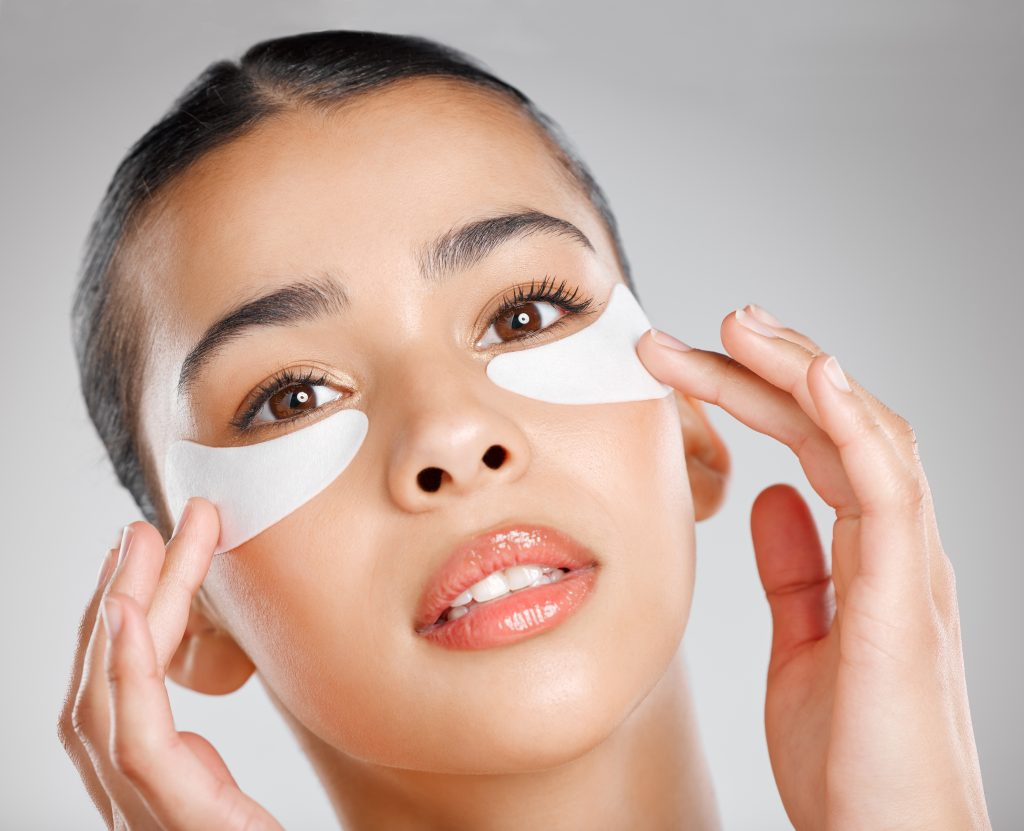 Studio shot of an attractive young woman wearing an under eye patch against a grey background.