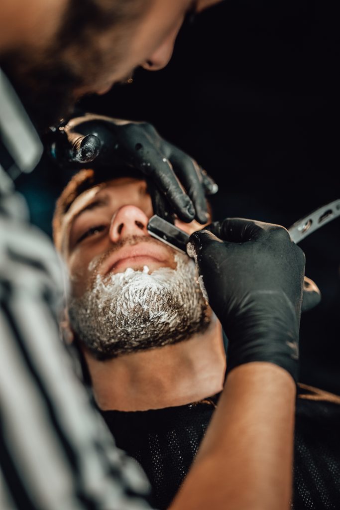 Close up of man shaving by professional stylist with dark gloves and blade in old fashioned retro barbershop. Step 8: Final Grooming Tips.