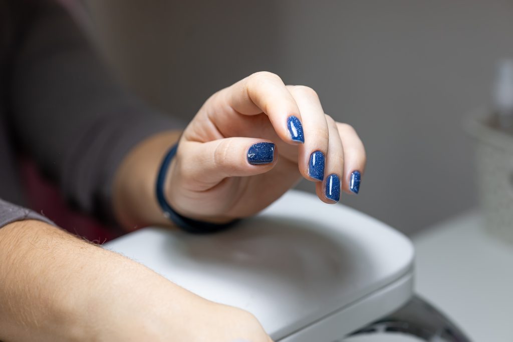 the client holds his hand on a stand with a blue gel polish applied to the nails. nail polish.