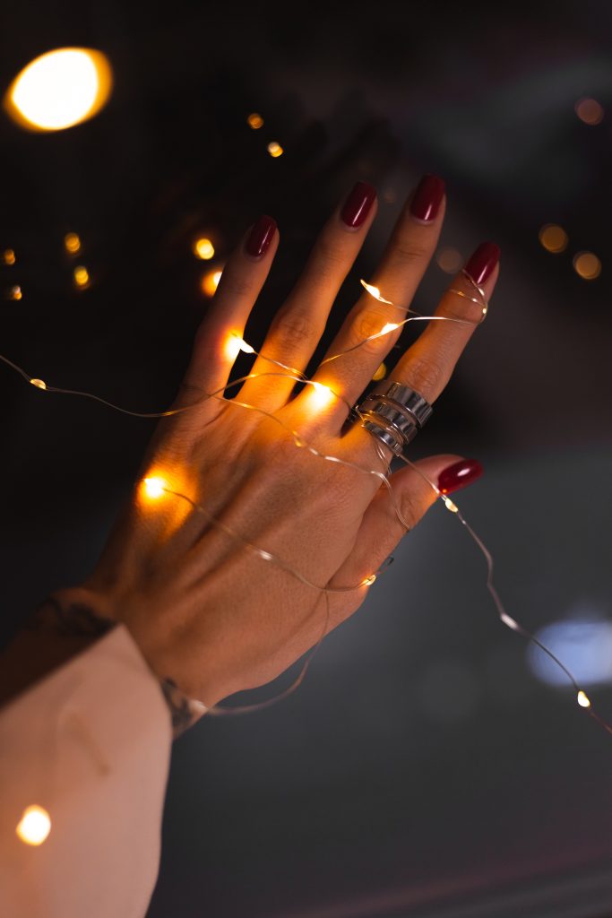 Beautiful dark photo of woman's hand fingers with big silver ring on background of flowers and glowing lights. Keeping Your New Year Nails Fresh and Vibrant.