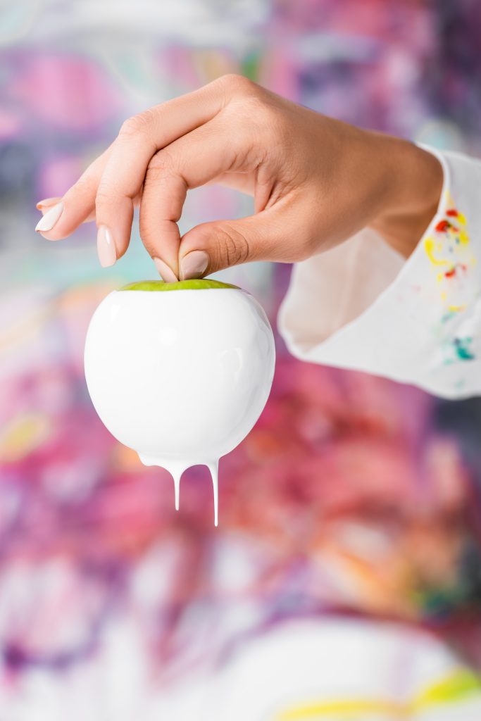 close up of female hand holding white painted apple. Tips to Keep Long and Healthy Nails. Beige painted nails.