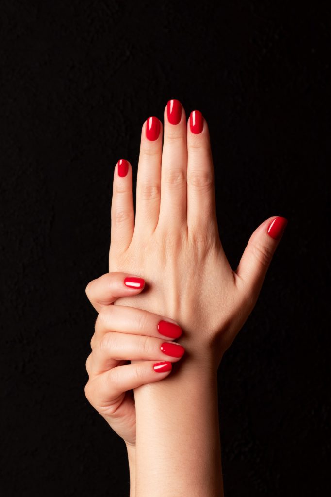 Female hands with beautiful manicure - red nails on dark black background. Nail, skin care concept