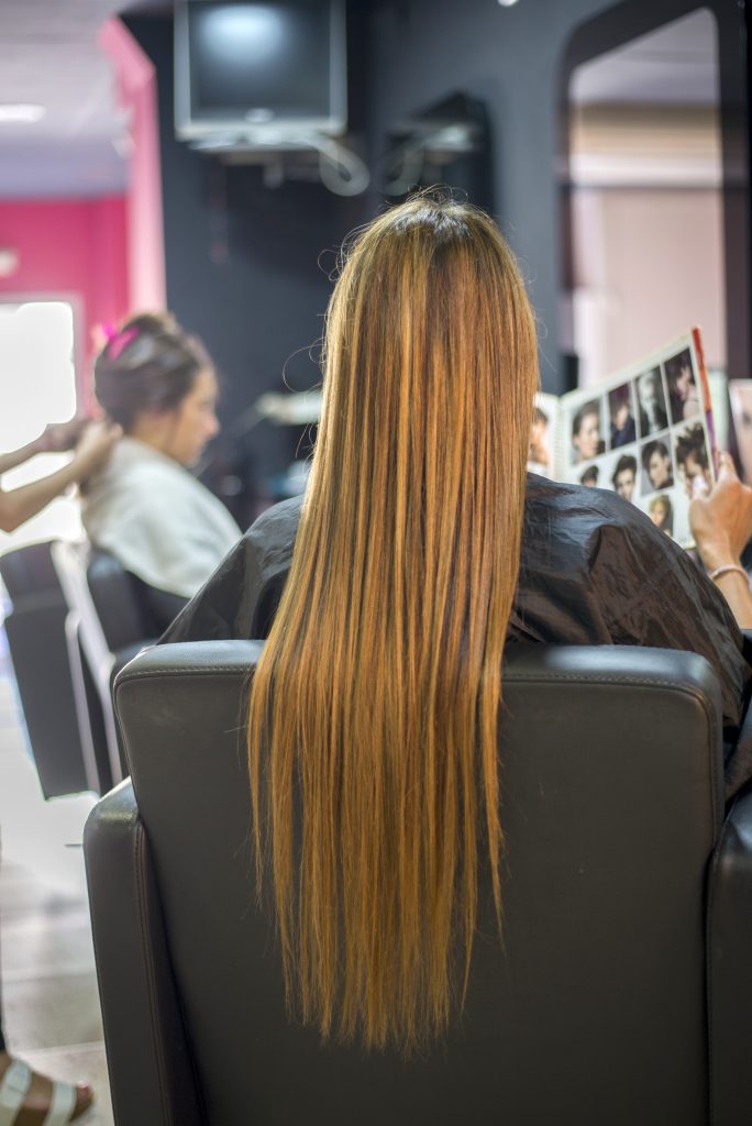 Hair Growth Solutions. Product Recommendations. Rear view of woman sitting on hairdresser chair choosing a hairstyle from the catalog