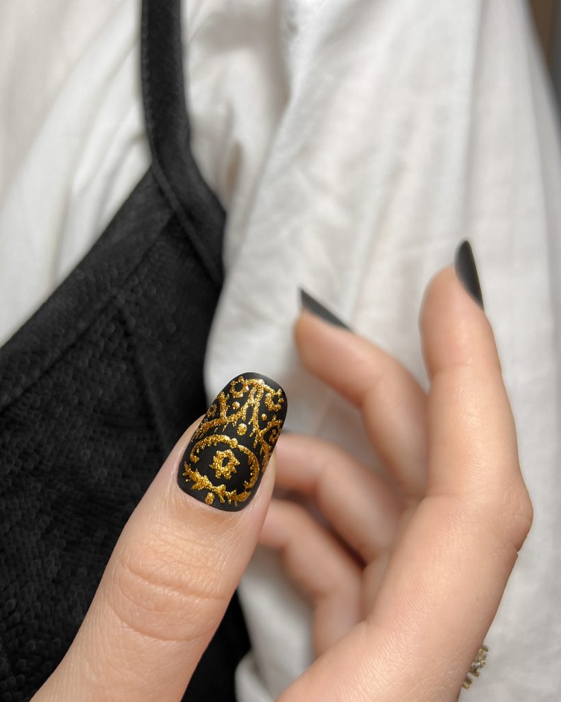 A hand showcasing nails with golden patterns. Trends in New Year Nail Art.