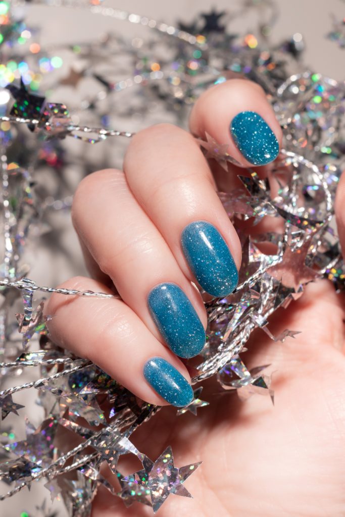 DIY Tips for Stunning New Year Nail Art. Female hand with beautiful holiday manicure - blue glitter nails with silver twisted wire with stars. Nail care concept.