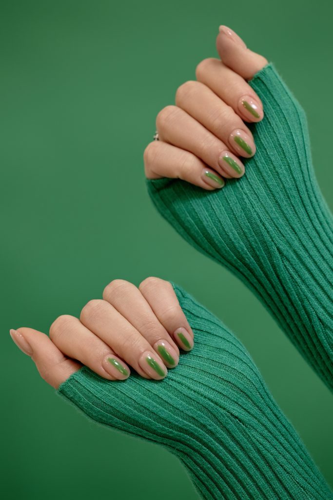 Vertical studio shot of green background with female hands in sweater of matching color. Seasonal Trends - Nail Styles Through the Year.