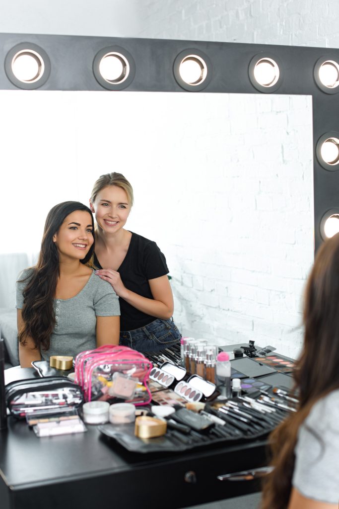 Makeup Courses in Canada. mirror reflection of beautiful young woman and smiling makeup artist. Benefits of Makeup Courses.