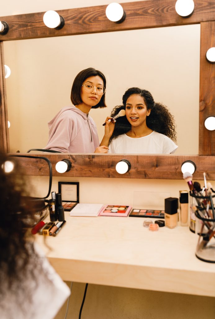 Makeup Courses in Canada. Model and makeup artist looking at a mirror preparing for a photo shoot. reputable platforms offer top-tier online makeup courses across Canada.