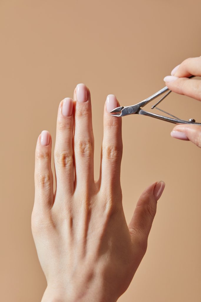 Daily Nail Care Routine for Healthy Nails. Partial view of woman using cuticle nipper isolated on beige. nail treatment. nail care. nails. home nail care.