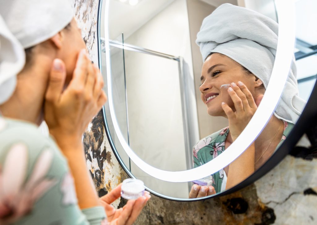 Nighttime Skincare. A smiling woman applies facial cream in her bathroom as part of her healthy morning routine. Facial care. night facial care.