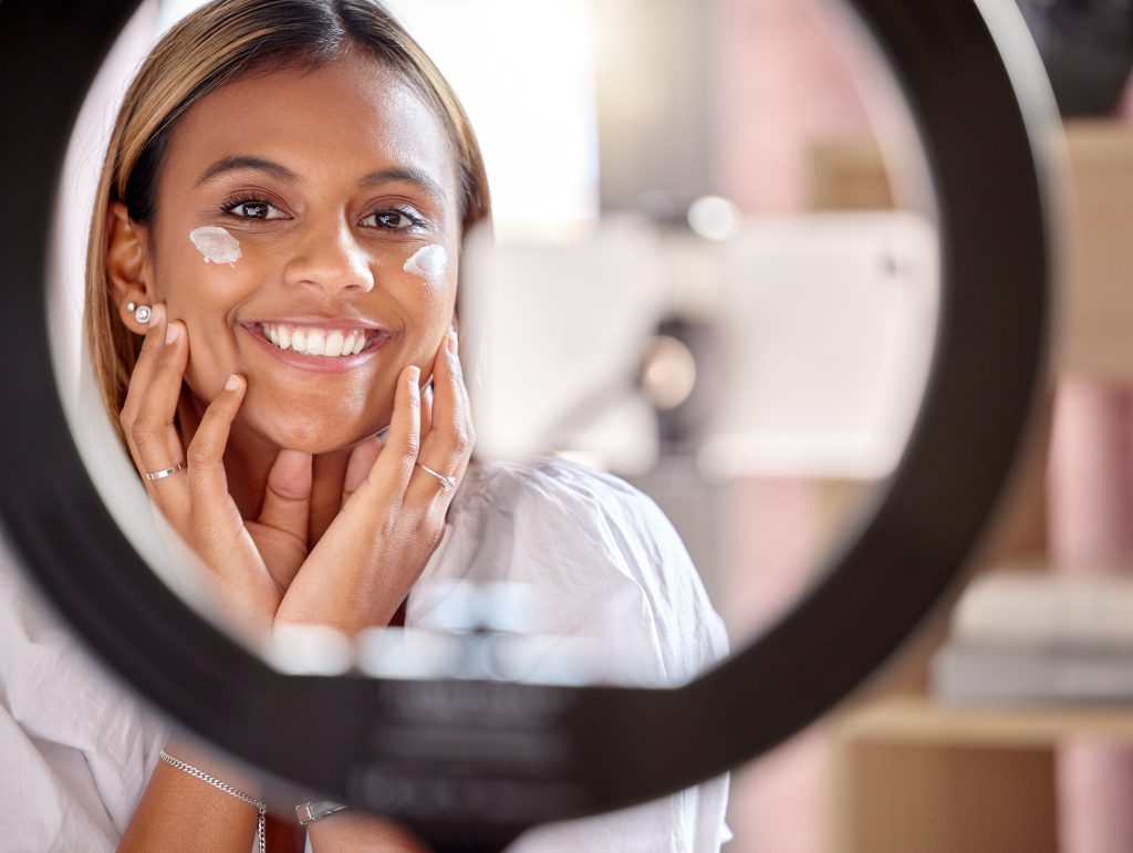 Black woman influencer, skincare cream and streaming tutorial for portrait, smile and beauty. Morning and Evening Eye Care Routine.