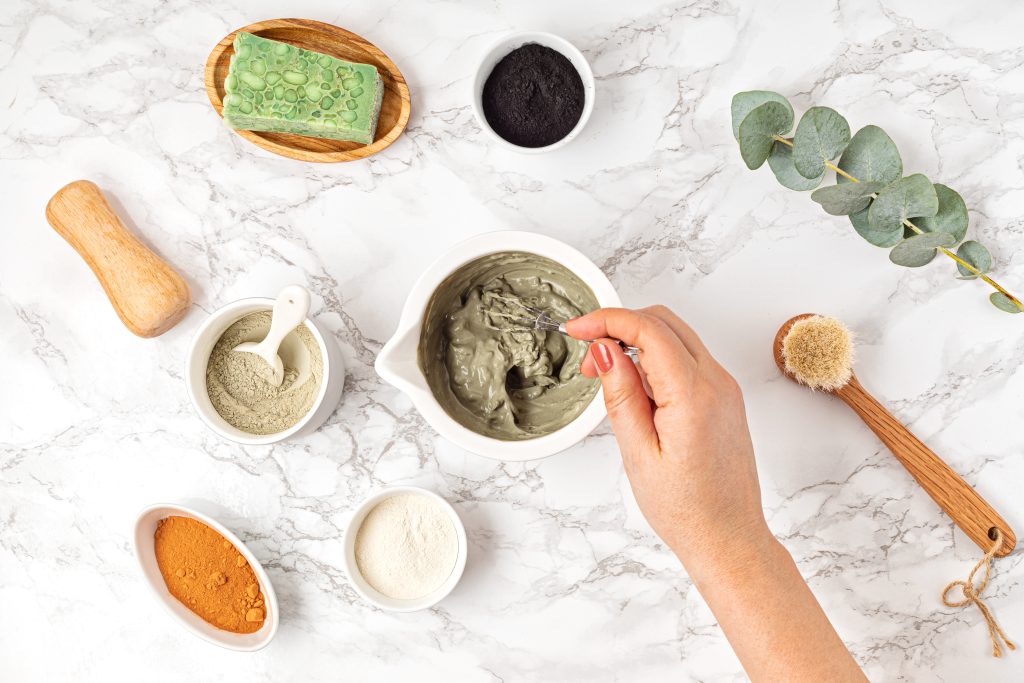 Home spa care for the skin of hands and nails. A young woman does a hand massage with a homemade coffee scrub with olive oil on marble background. Top view.  Homemade clay facial mask. Zero waste eco friendly diy beauty products ingredients on light background, flat lay, top view