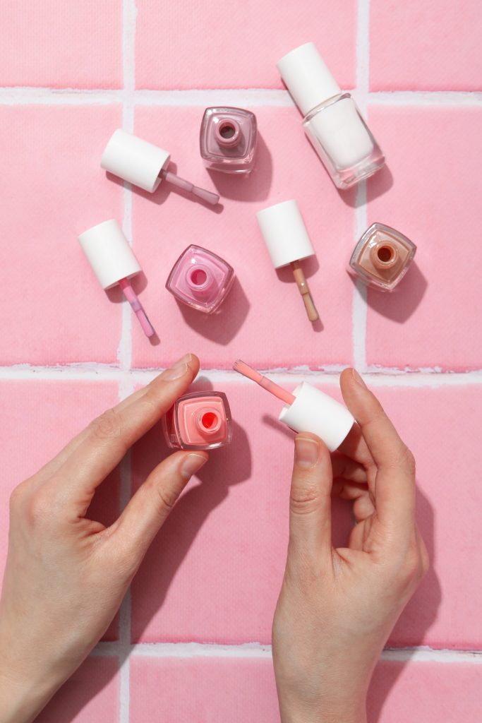 Nail polishes in female hands on pink background, top view. nail lacquers. nail polishes. 