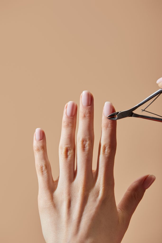 Partial view of woman doing manicure using cuticle nipper isolated on beige. Tools and Products to Include in Your Nail Care Kit.