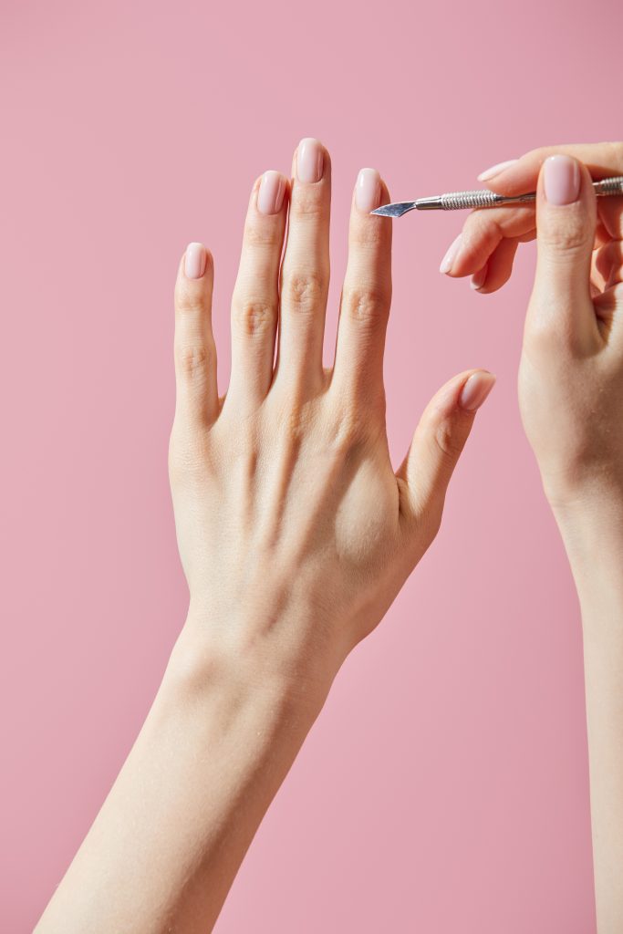 Partial view of woman doing manicure with cuticle pusher isolated on pink. DIY Nail Care Routines.