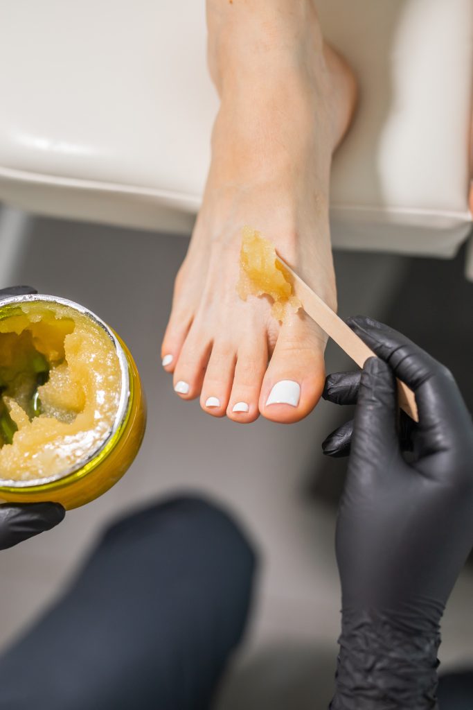 Woman doing foot peeling in pedicure SPA salon. Sugar scrub and relax beauty procedure.