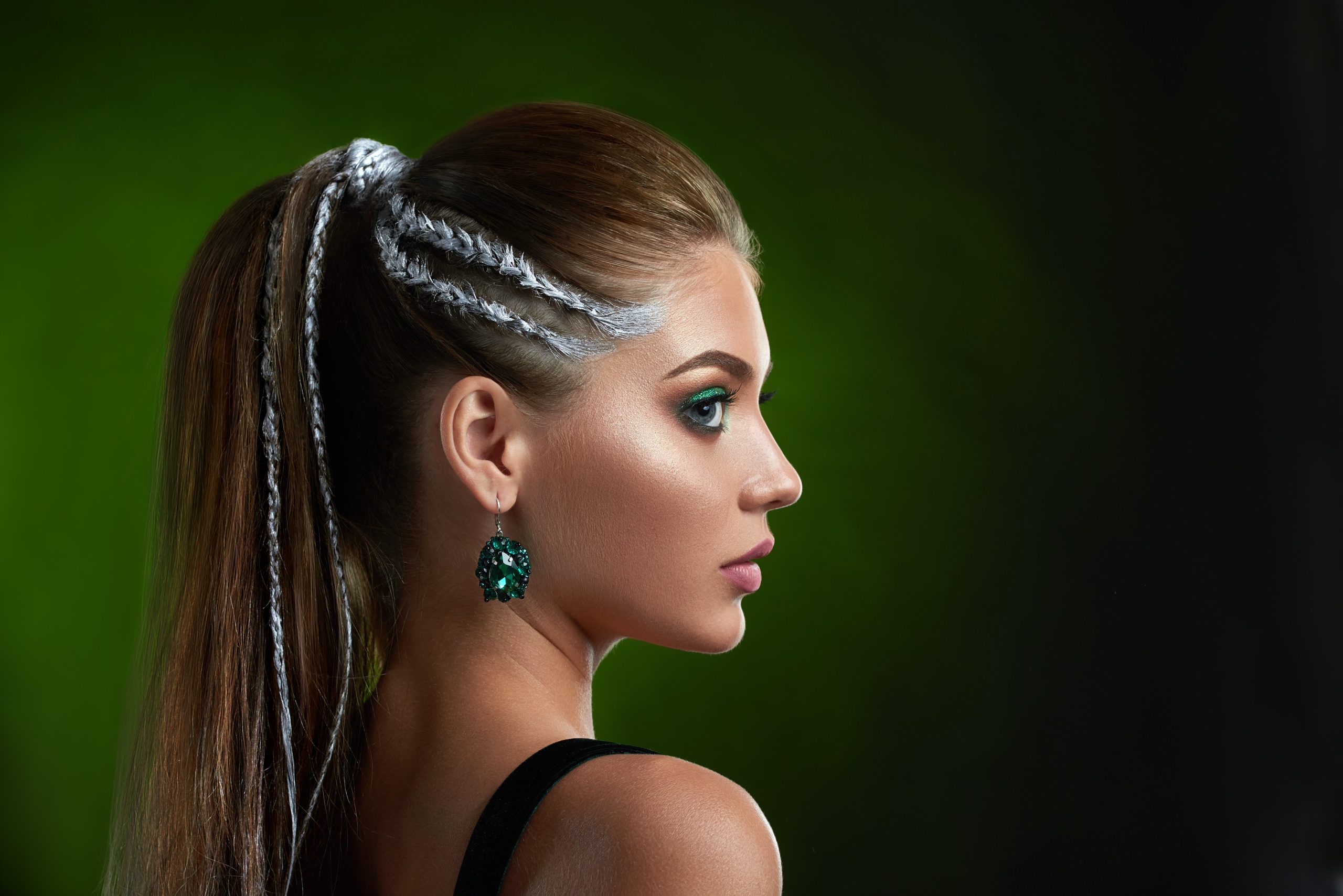 top 2025 hair trends. Beautiful female with stylish hairstyle after beauty salon, perfect bronze skin, long eyelashes, makeup in green colors. Seductive woman posing at studio against green background. Concept of beauty.