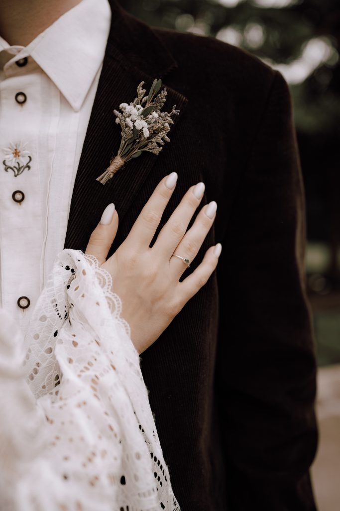 Bride's hand lying on groom's suit with buttonhole. Boho wedding details.