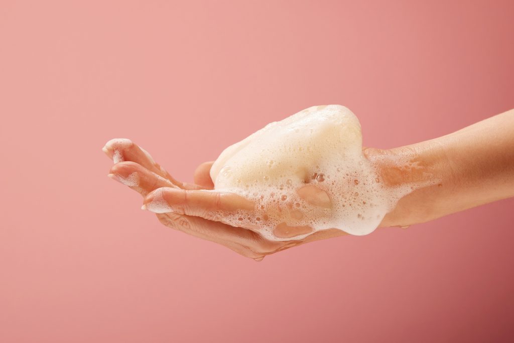 A close-up shot of hands with soap and foam on bright pink background