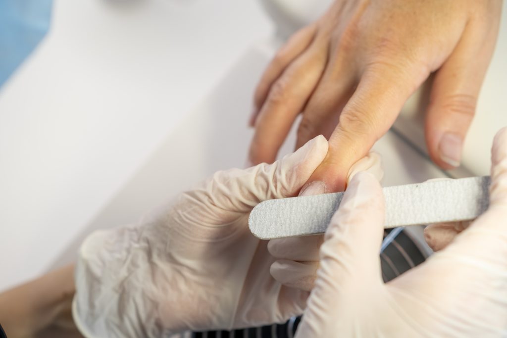 Nail care procedure in a beauty salon. Female hands and tools for manicure, process of performing manicure in beauty salon. Gloved hands of a skilled manicurist cutting cuticles. Concept spa body care. Quick Fixes for Peeling Nail Polish.